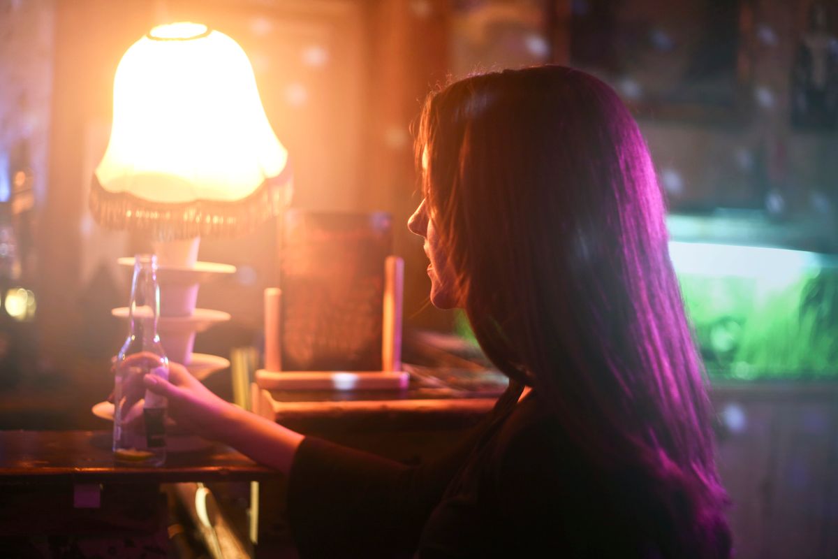Moody bar scene featuring a woman holding a beer bottle under warm lamp light.