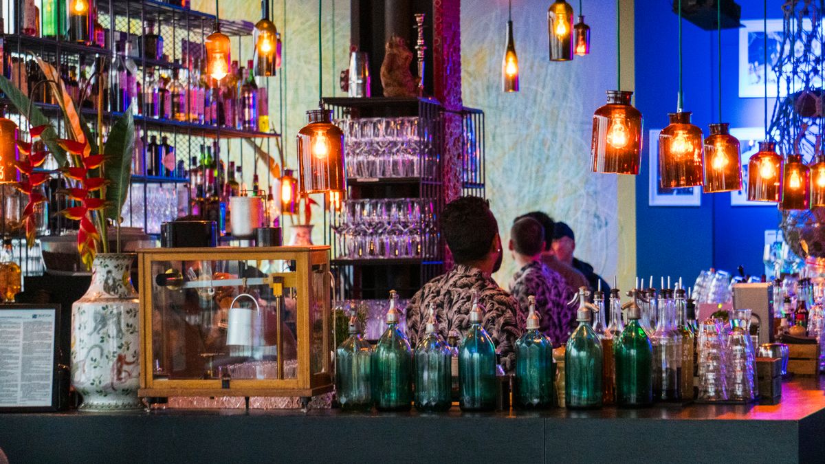 A lively bar scene with colorful bottles, hanging lights, and people enjoying a night out.