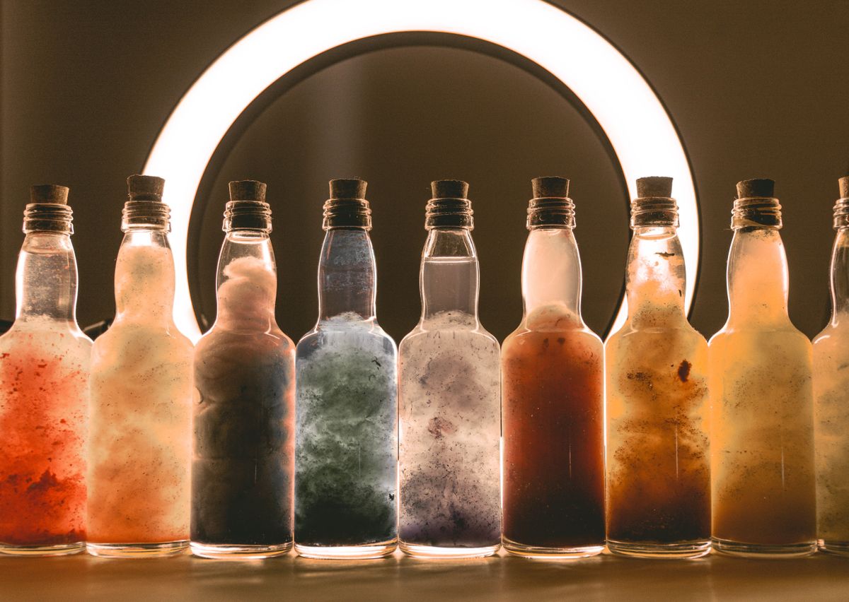Variety of colorful bottles with cork stoppers, illuminated by a ring light, creating an artistic still life.