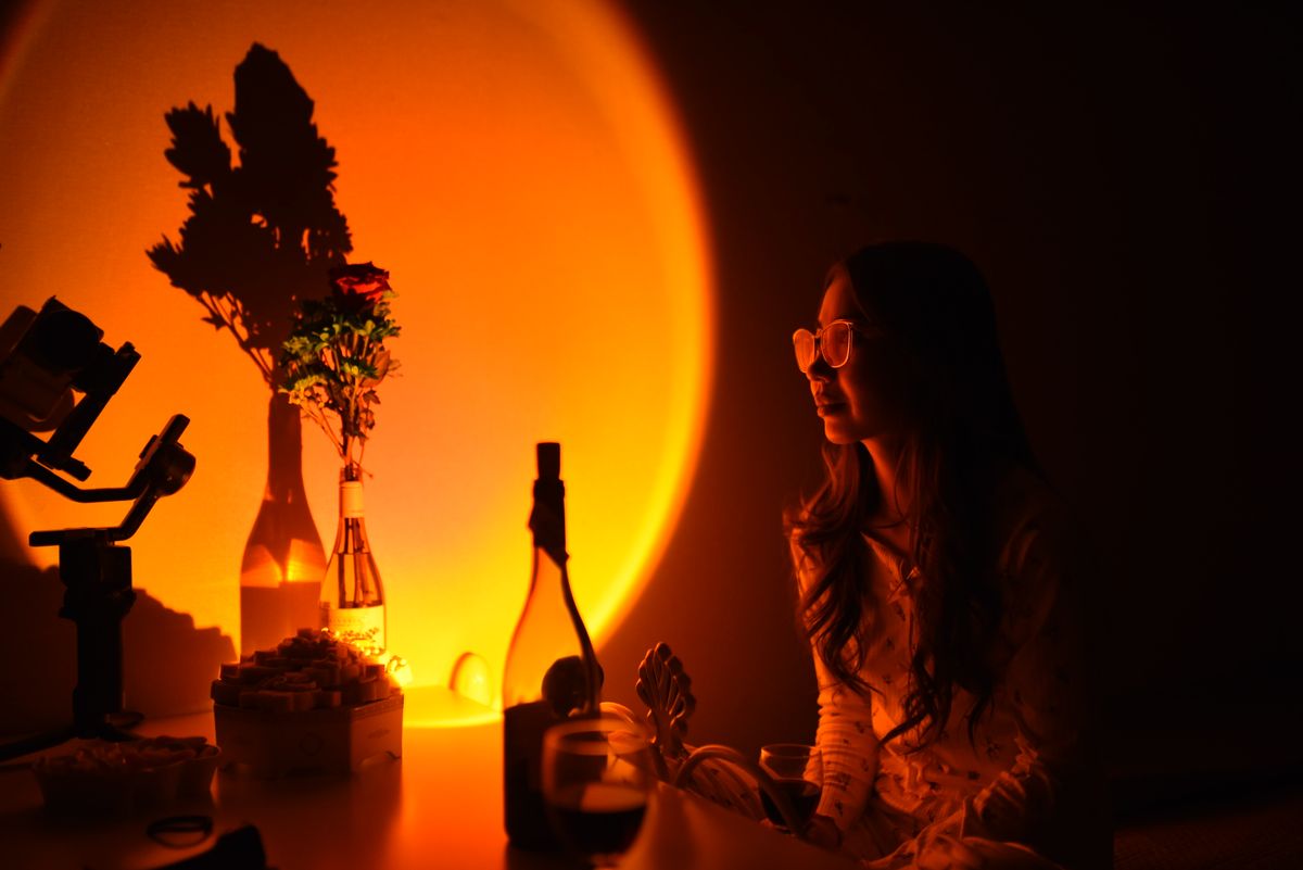 A woman enjoying a tranquil evening with warm orange lighting and floral shadows.