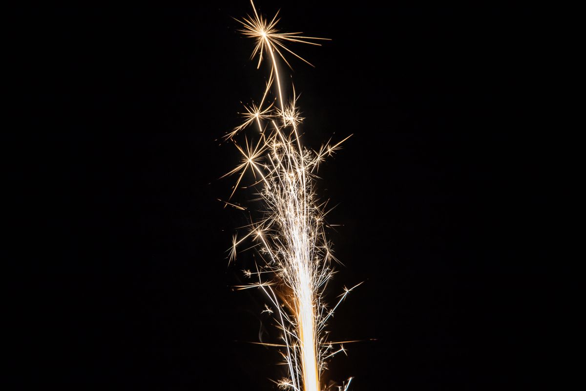A vibrant sparkler illuminates the night sky with bright sparks and festive light.