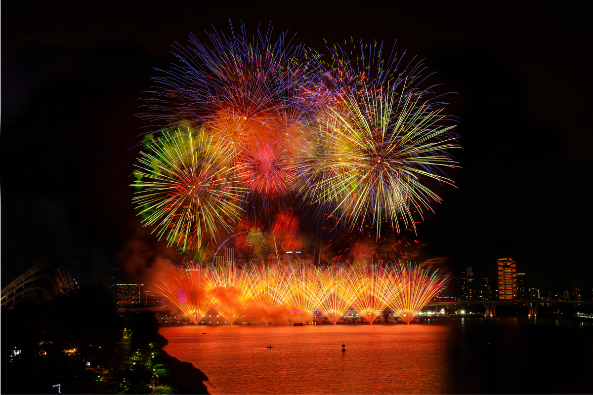Vibrant fireworks light up the night sky over a cityscape and waterfront, creating a mesmerizing display.