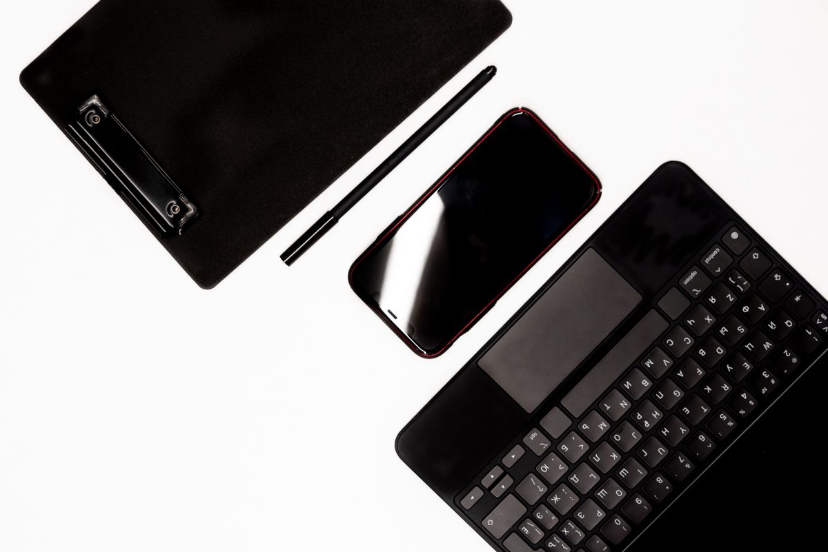 Flat lay of modern devices including a smartphone, tablet, pen, and keyboard on a white surface.