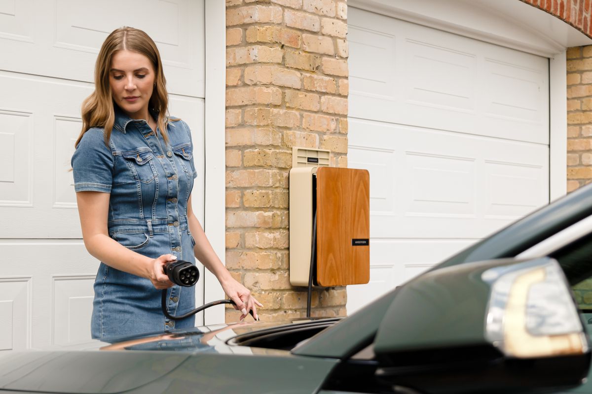 A woman plugs in an electric vehicle charger at a home charging station.