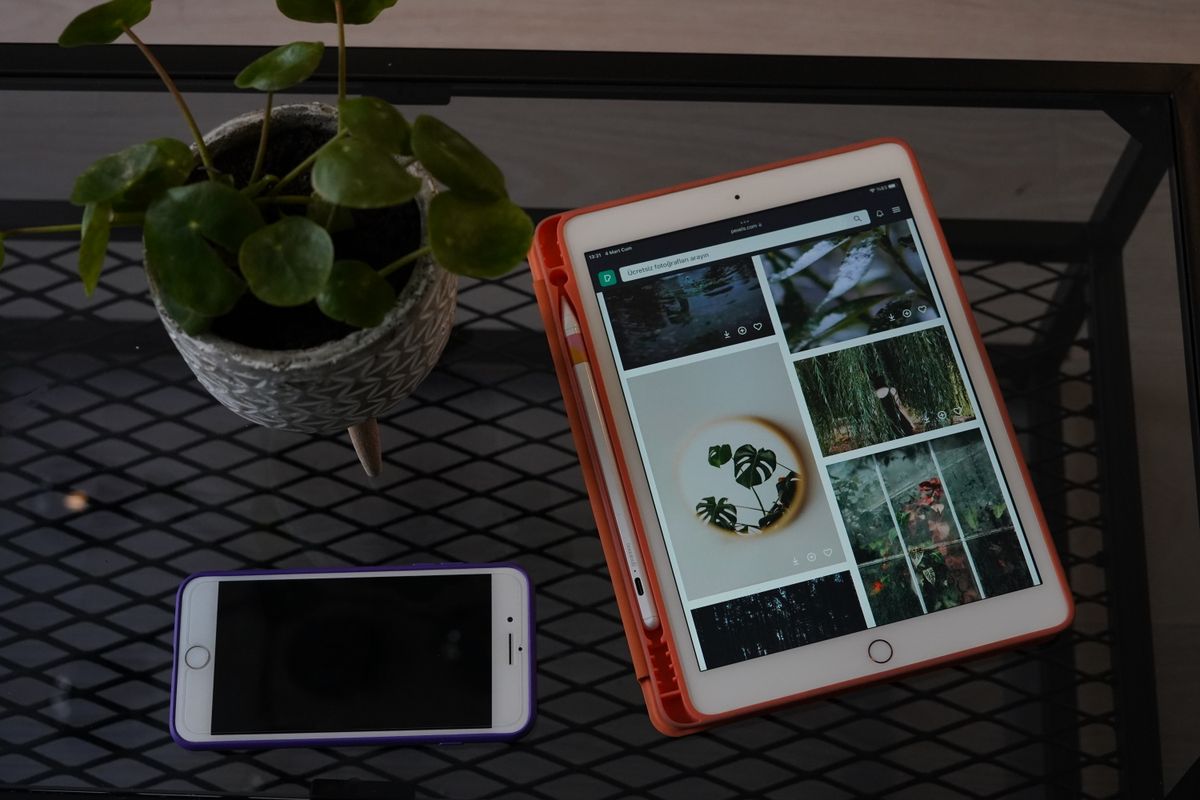 A tablet and smartphone on a metal desk next to a potted plant, showcasing modern technology.