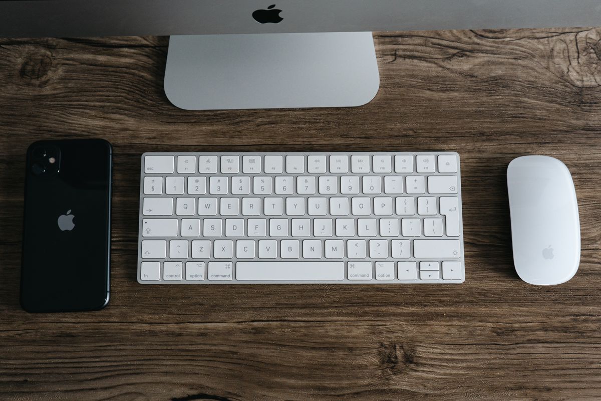 A minimalist workspace featuring a smartphone, keyboard, and mouse on a wooden desk.