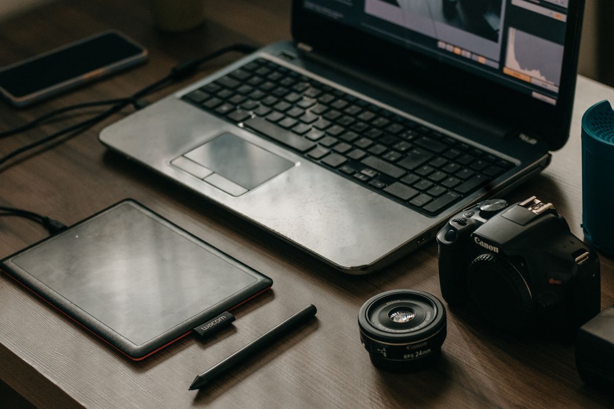 Laptop, camera, lens, and graphic tablet on a desk for digital creatives.