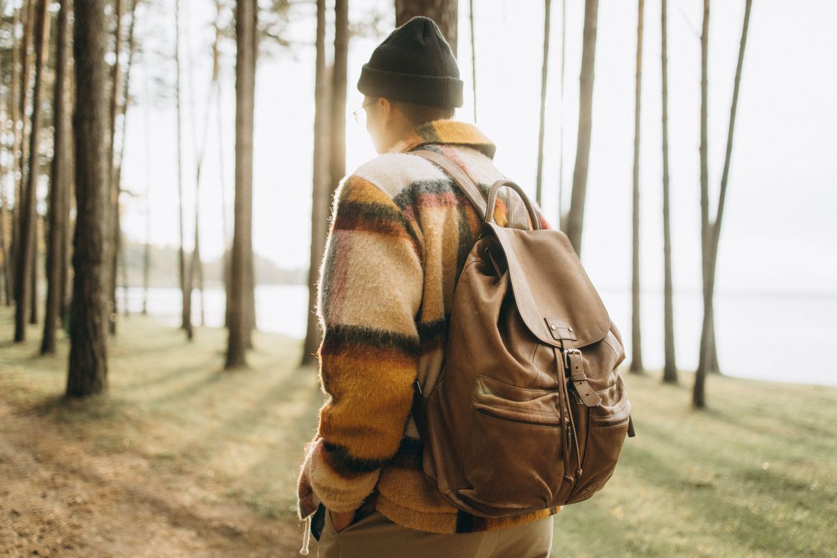 A man with a backpack walks through a serene autumn forest, capturing a moment of peaceful travel.