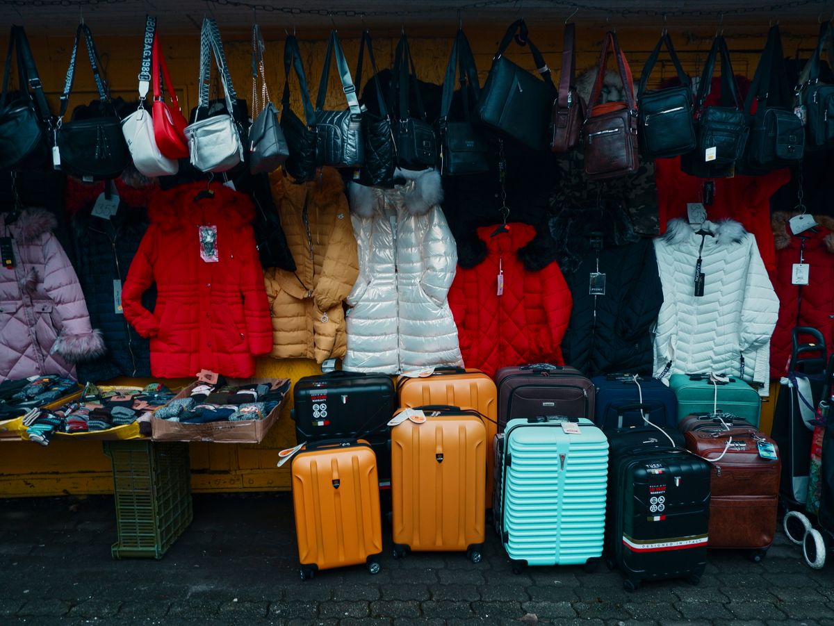 Colorful winter jackets and luggage on display at an outdoor market stall showcasing diverse merchandise.