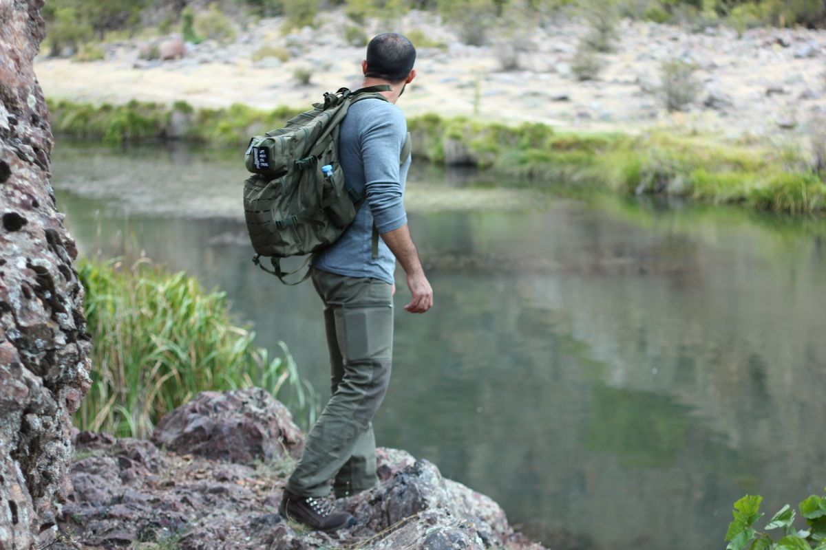 A man with a backpack stands by a peaceful river, embracing the beauty of nature.