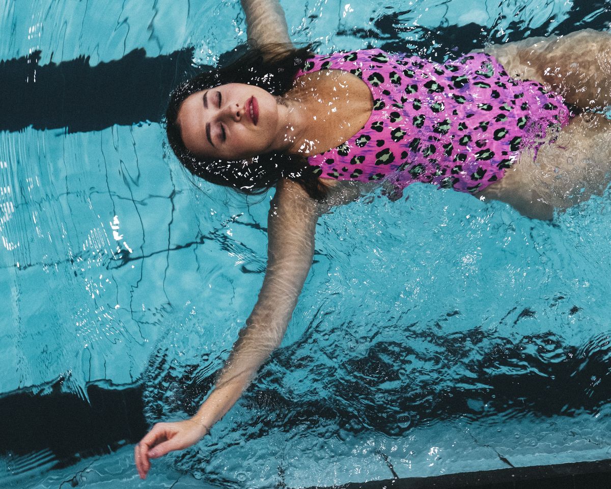 Woman in a pink leopard swimsuit floating peacefully in a swimming pool.