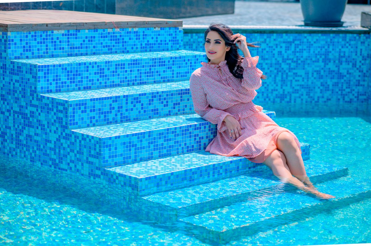 Elegant woman in a pink dress sitting on poolside steps, enjoying a sunny summer day.