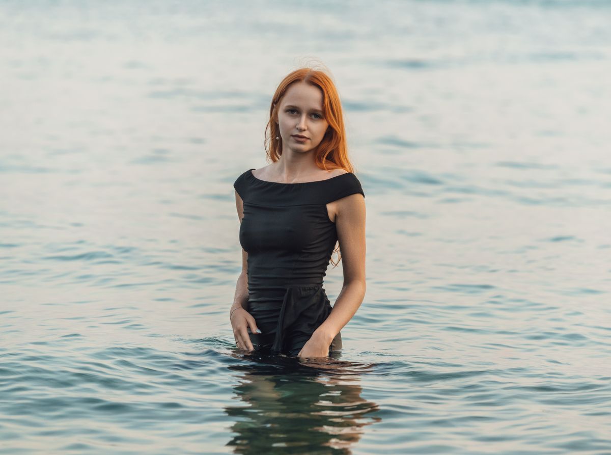 Woman standing in the sea wearing a black dress, serene water background.