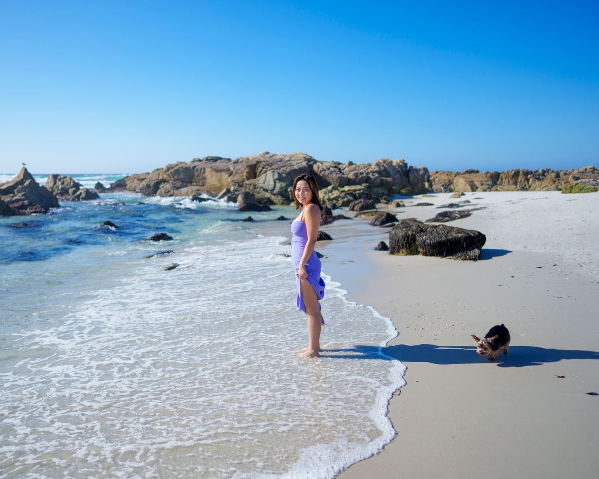 A woman in purple stands on a sunny day at Monterey beach, enjoying the ocean breeze.