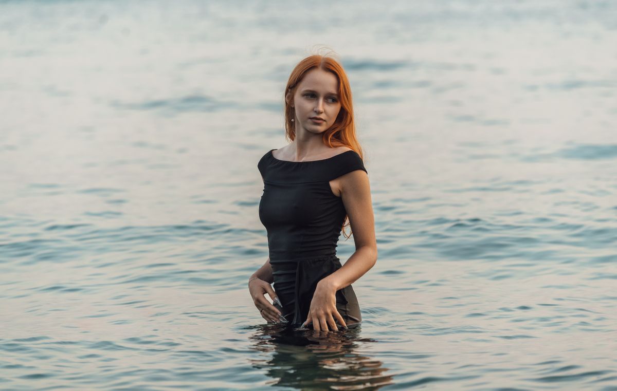 Stylish young woman standing in calm sea water with serene expression.