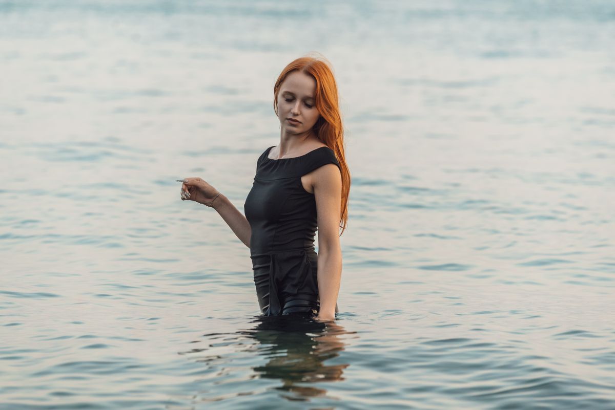 Woman in black dress standing in calm sea water, serene atmosphere.