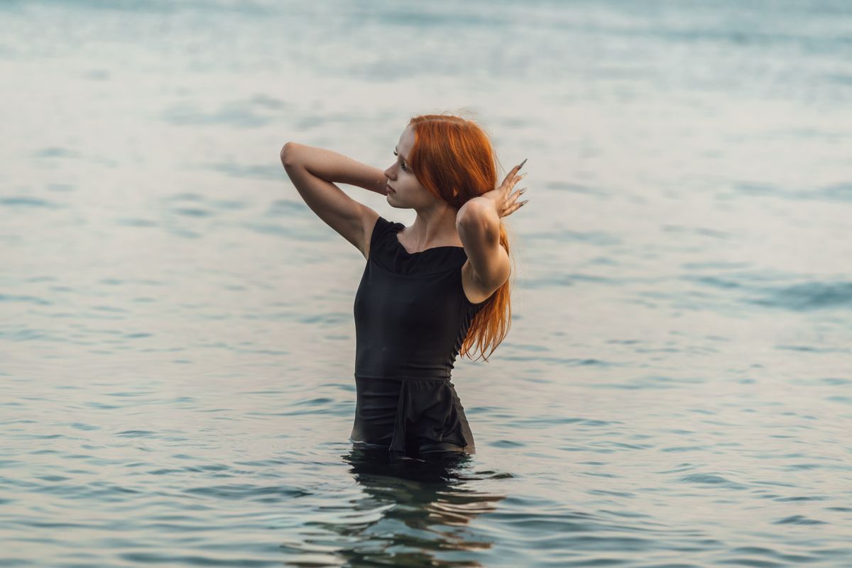 A woman in a black dress poses gracefully in water, capturing a serene, summer vibe.