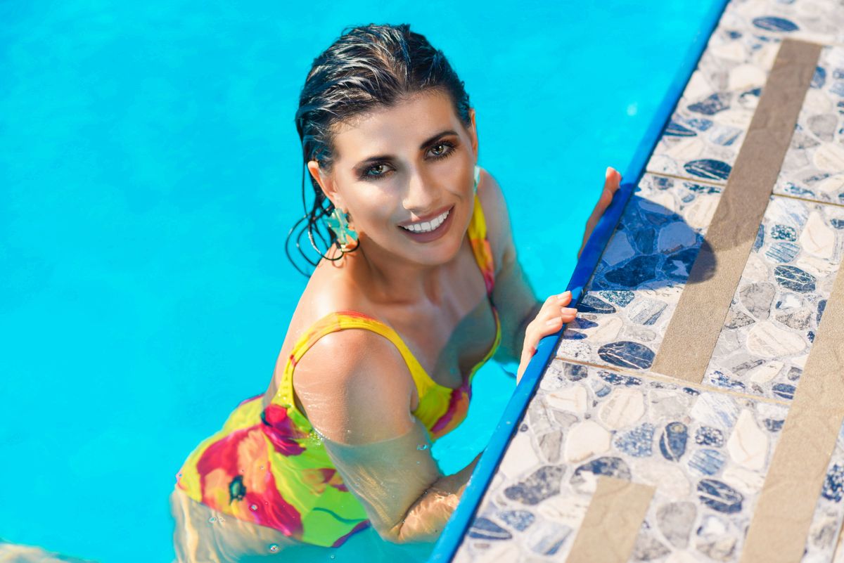 Vibrant portrait of a smiling woman in a colorful swimsuit enjoying poolside relaxation.