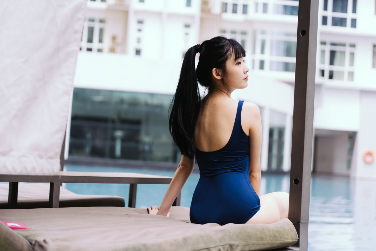 Elegant young woman in blue swimsuit sitting poolside, exuding relaxation and leisure.