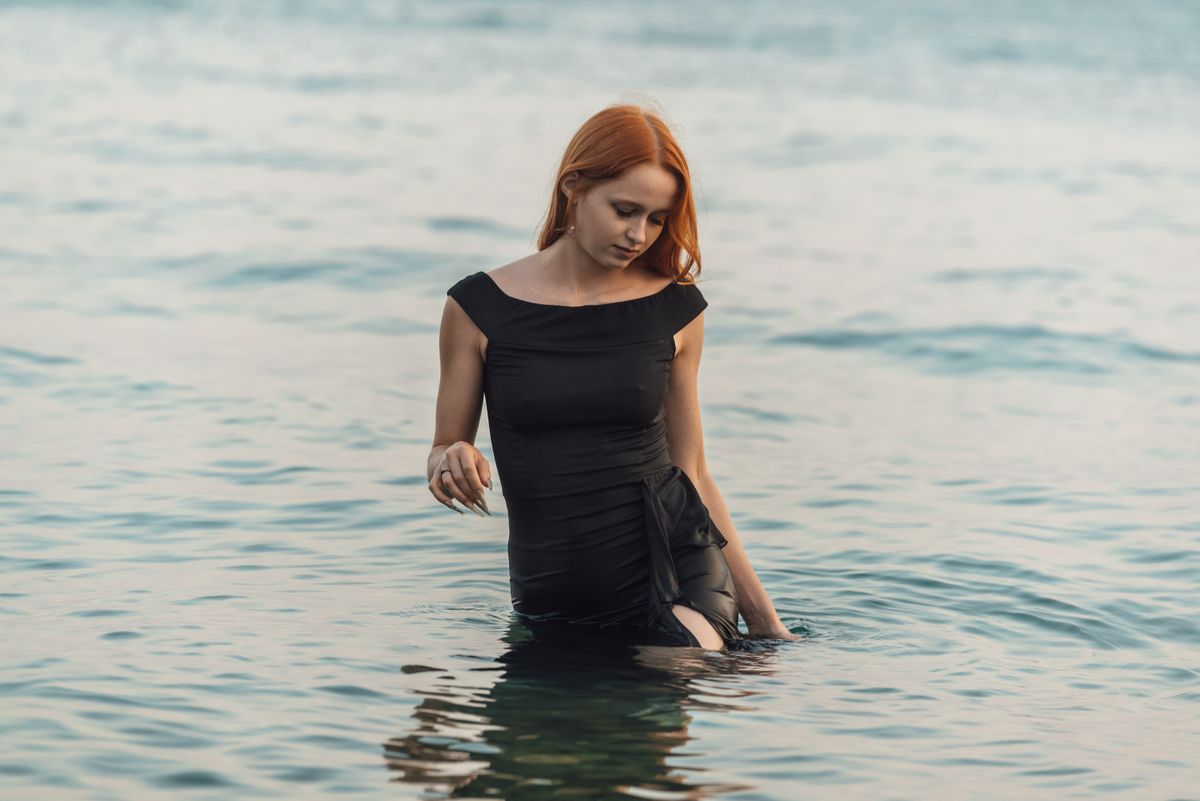 Young woman in black dress standing in sea, exuding peace and contemplation.