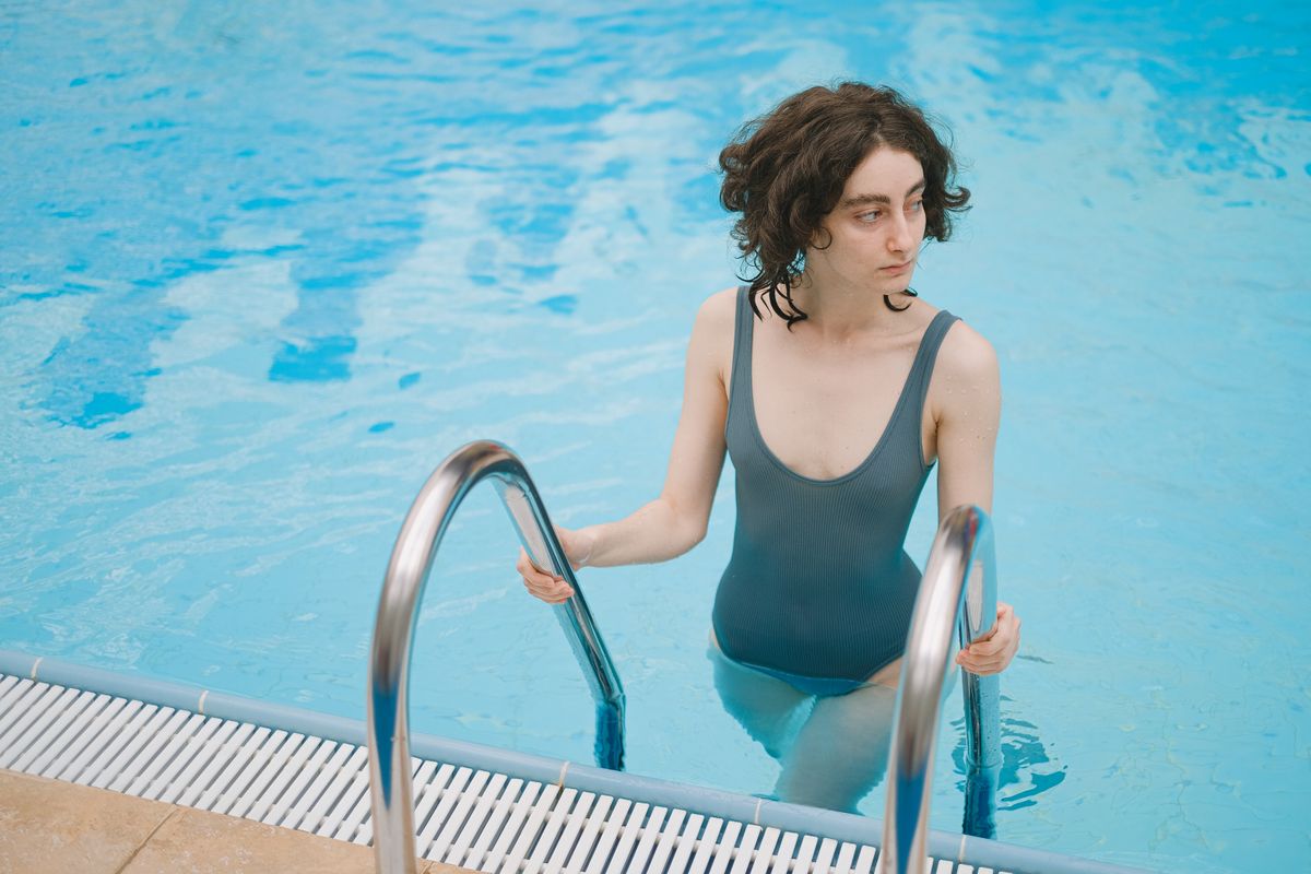 A woman wearing a one-piece swimsuit exits the swimming pool using a metal ladder.