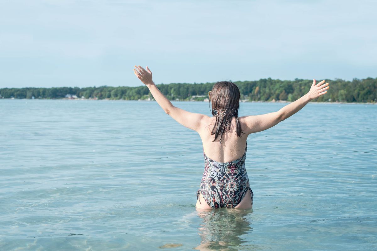 A woman in a swimsuit joyfully raises her arms in the tropical beach waters, embodying freedom and relaxation.