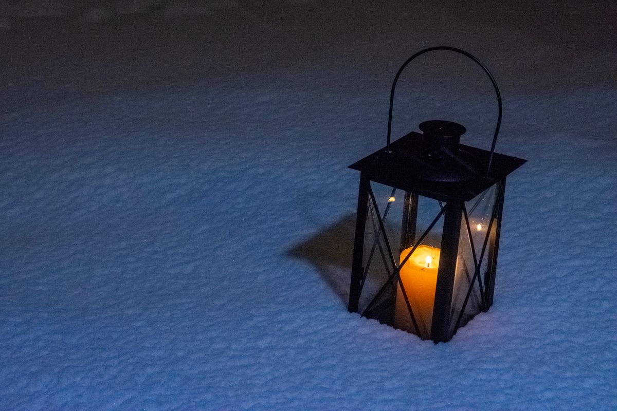 Illuminated lantern in snow casting a warm glow on a cold winter night outdoors.