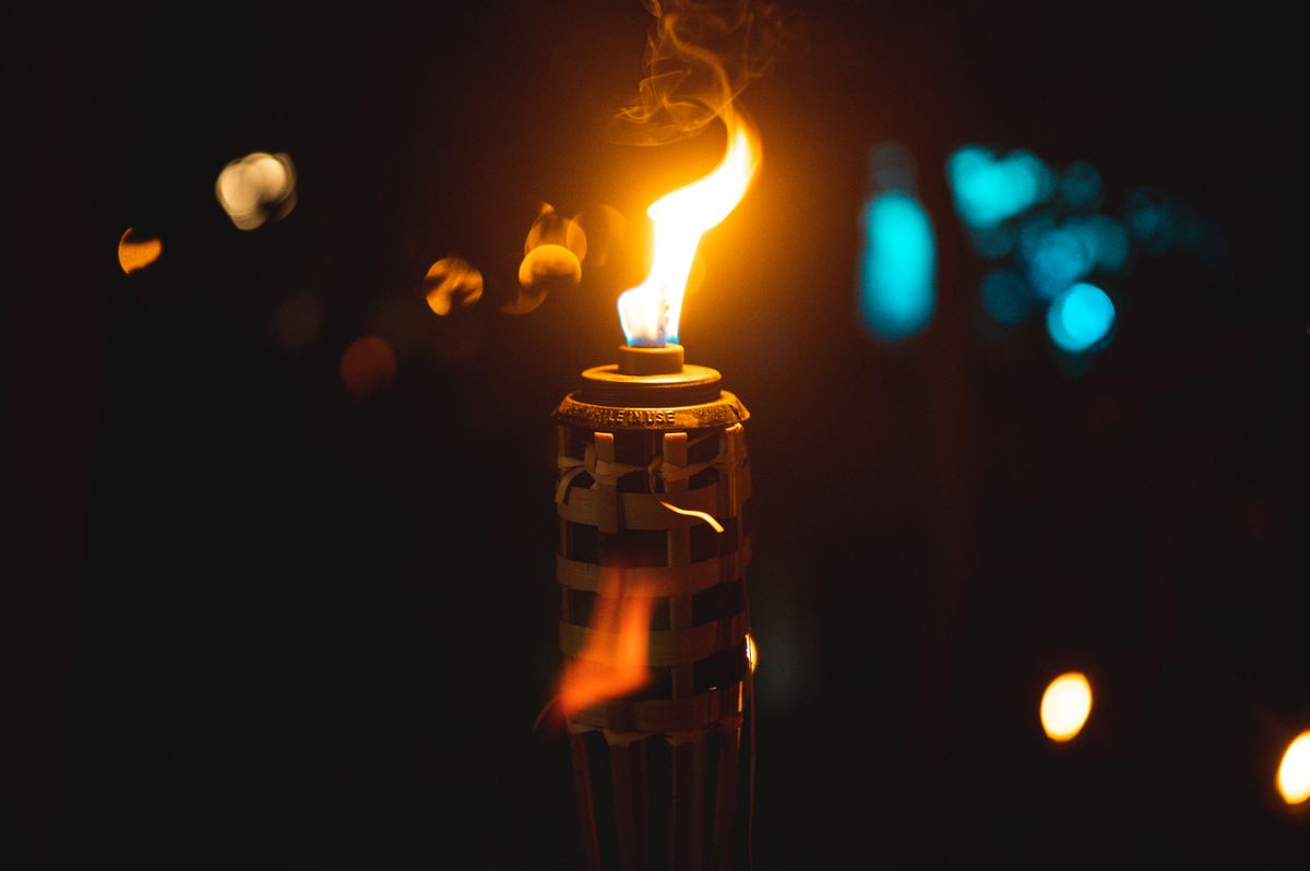 A close-up of an outdoor torch with a vibrant flame against a night backdrop, creating a warm ambiance.