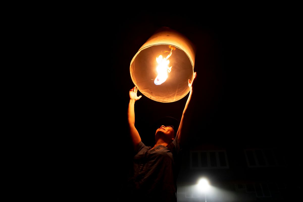 A person launches an illuminated sky lantern against a dark night sky, creating a warm glow.