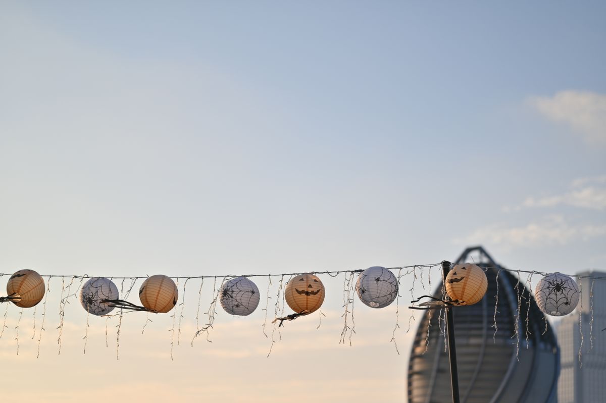 String lights with Halloween lanterns hanging outdoors against a city skyline in the evening.