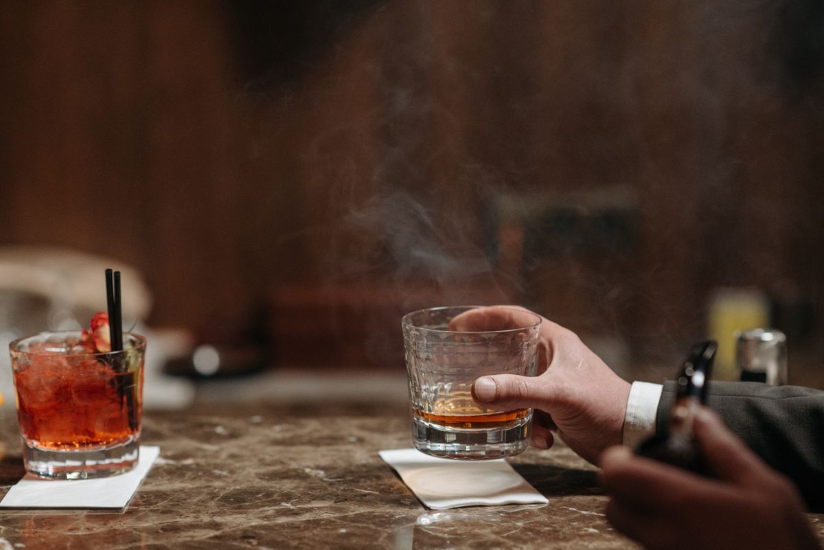 A sophisticated scene of a hand holding a whiskey glass at a bar with cocktails.