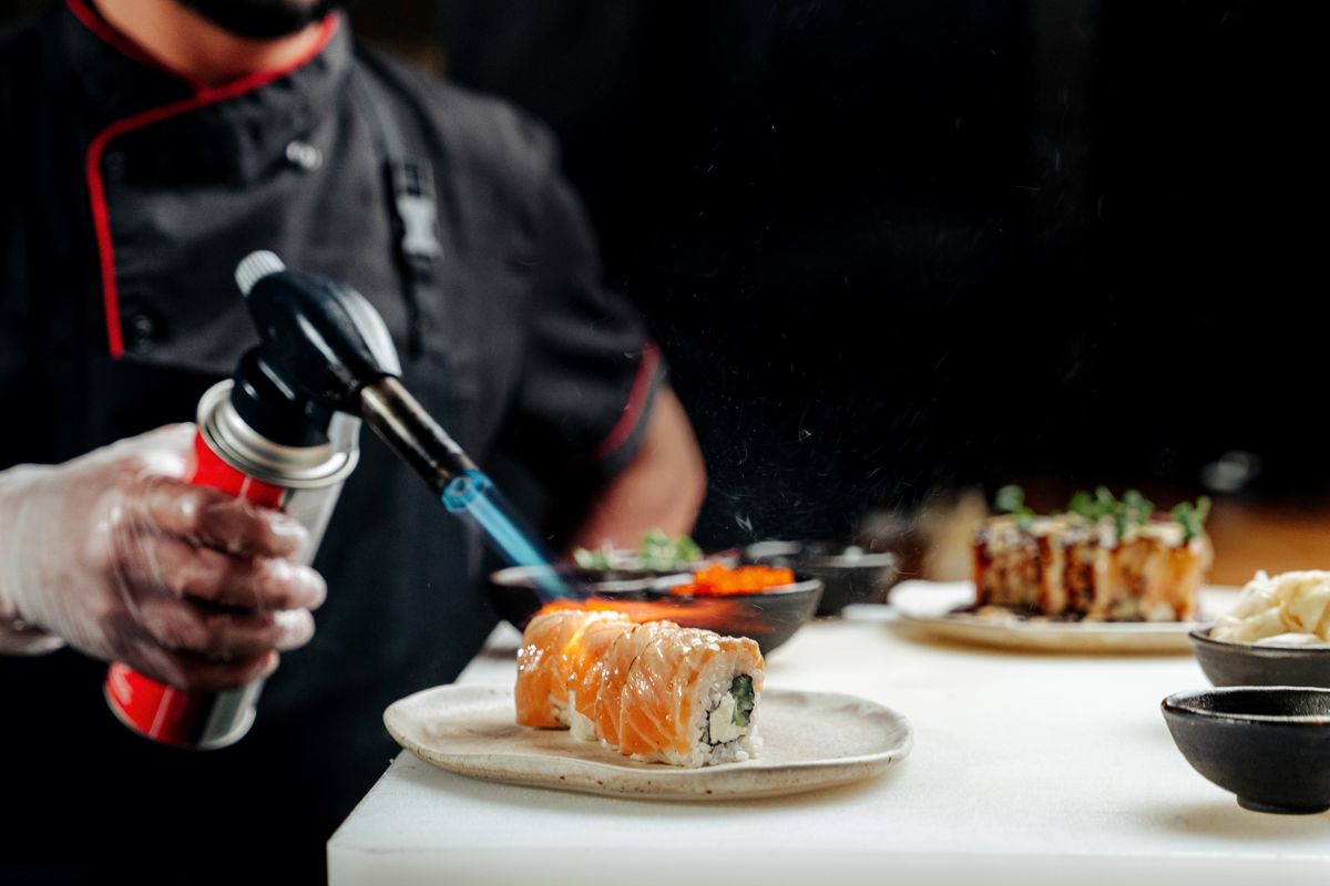 A chef skillfully uses a blowtorch to prepare sushi in a restaurant kitchen.