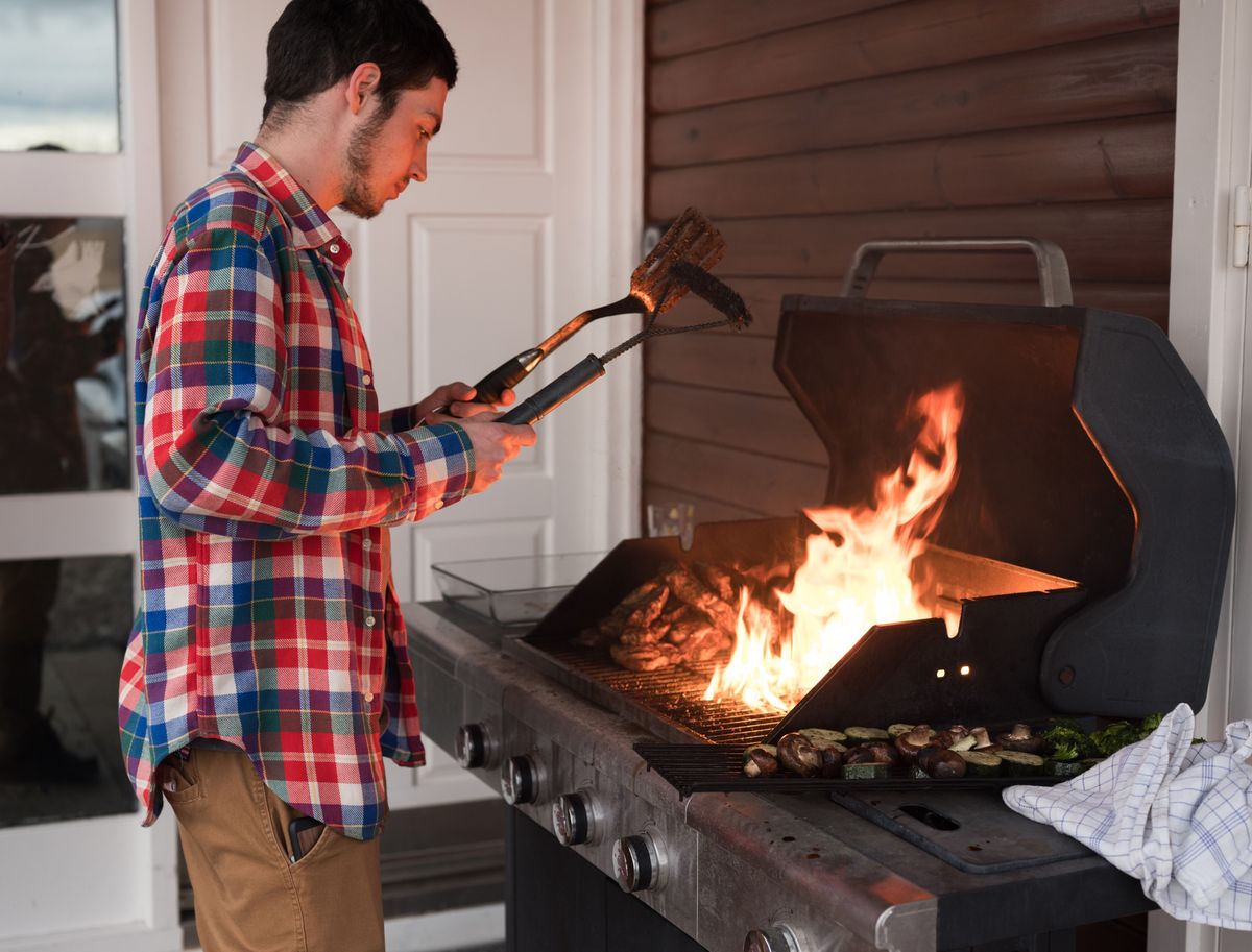 Man grilling outdoors with intense flames and vegetables on a barbecue grill.