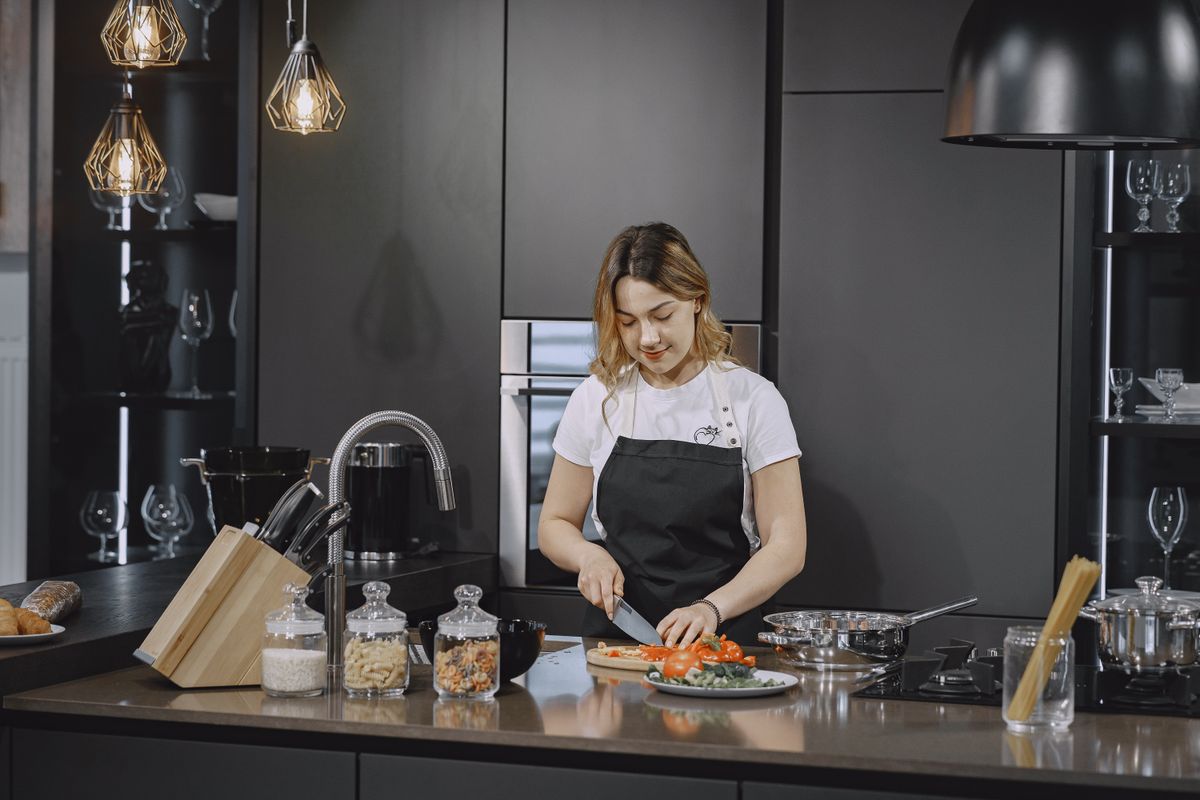 A woman slices vegetables on a kitchen counter under elegant lighting.