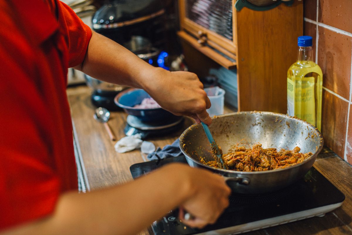 Person cooking shredded meat in a wok on a stove, home kitchen cooking scene.