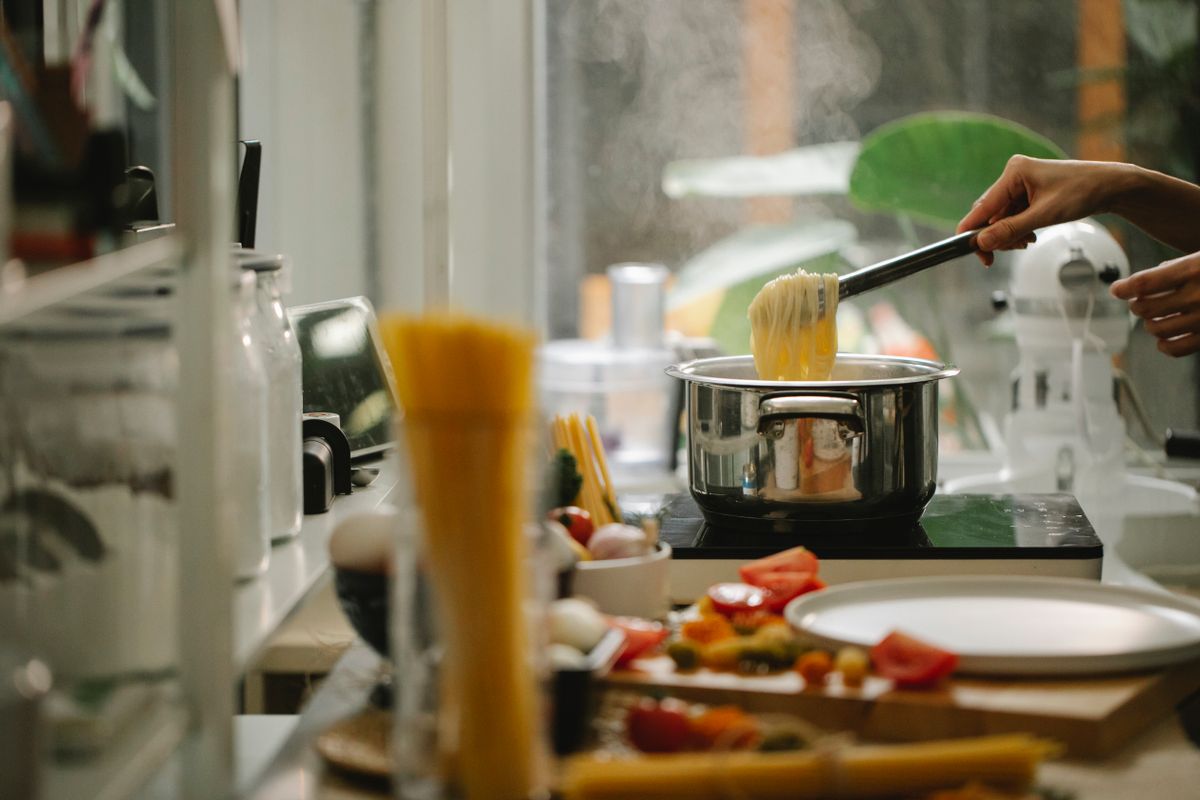 Crop anonymous housewife picking freshly cooked Italian spaghetti from saucepan while cooking and serving food in light kitchen