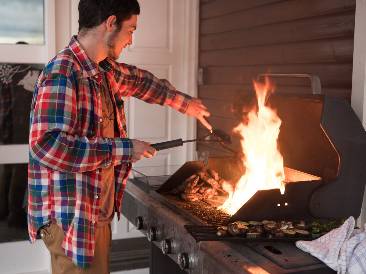 A man cooks meat and vegetables on a flaming outdoor grill, showcasing a vibrant barbecue scene.