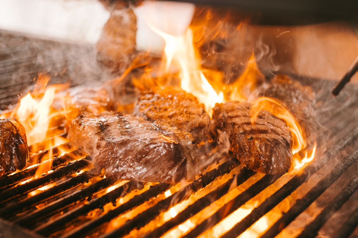 Juicy steaks cooking on a barbecue grill with flames and smoke rising.