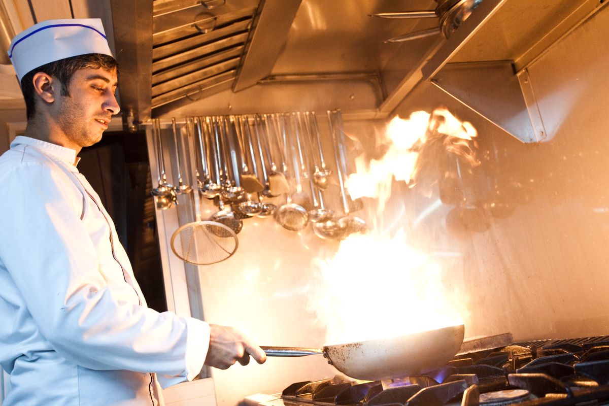 Dynamic shot of a chef flambéing a dish with skill and focus in a professional kitchen setting.