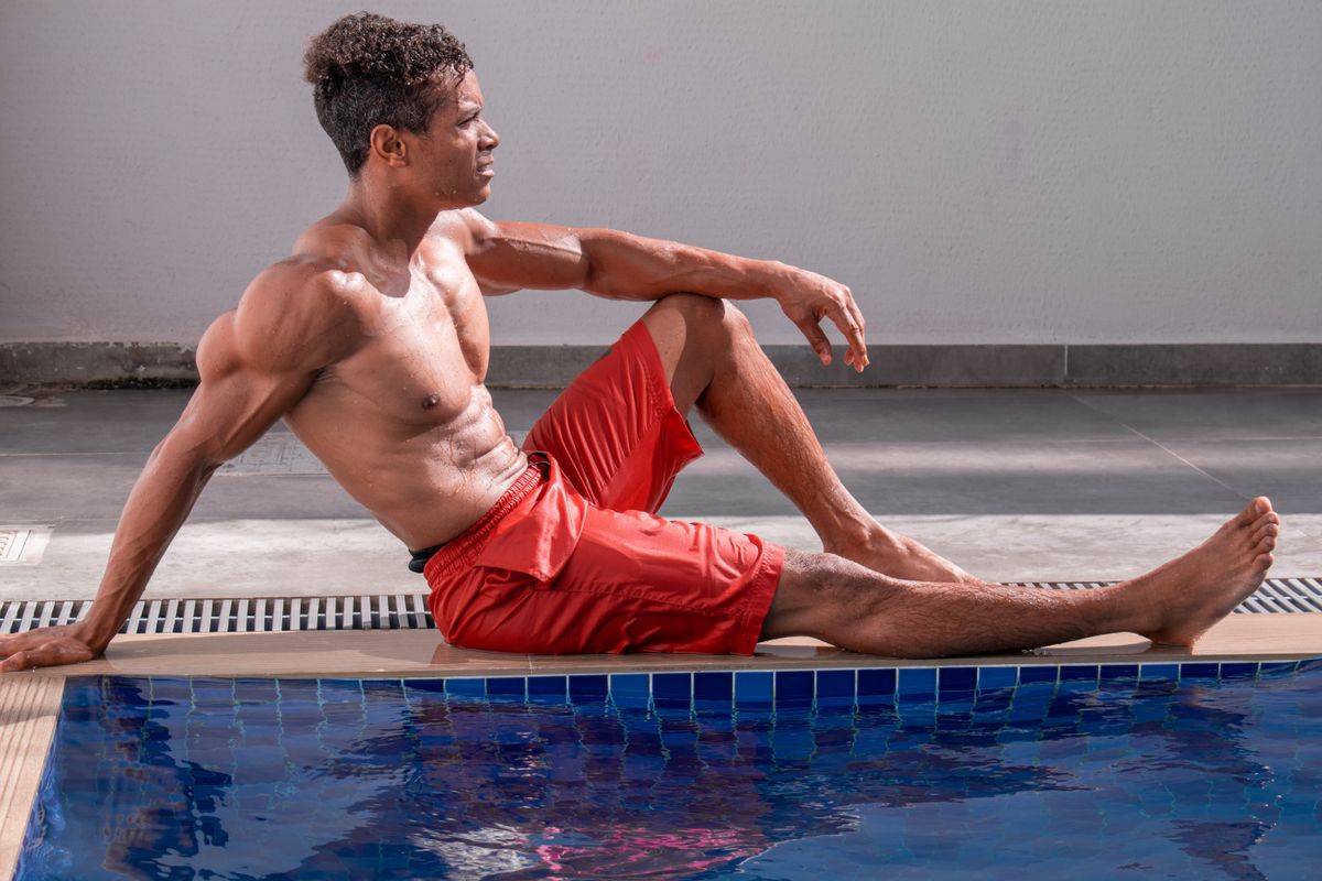 Athletic man relaxing by the pool wearing red shorts, enjoying a sunny day.