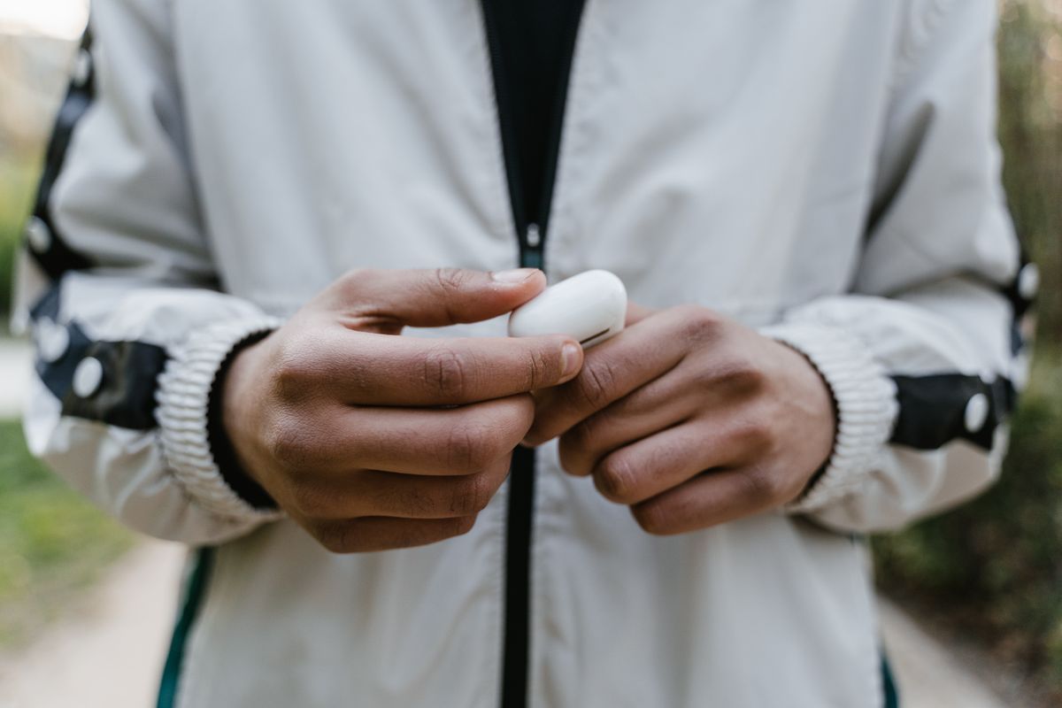 A person in a jacket holding a case of wireless earbuds outdoors.