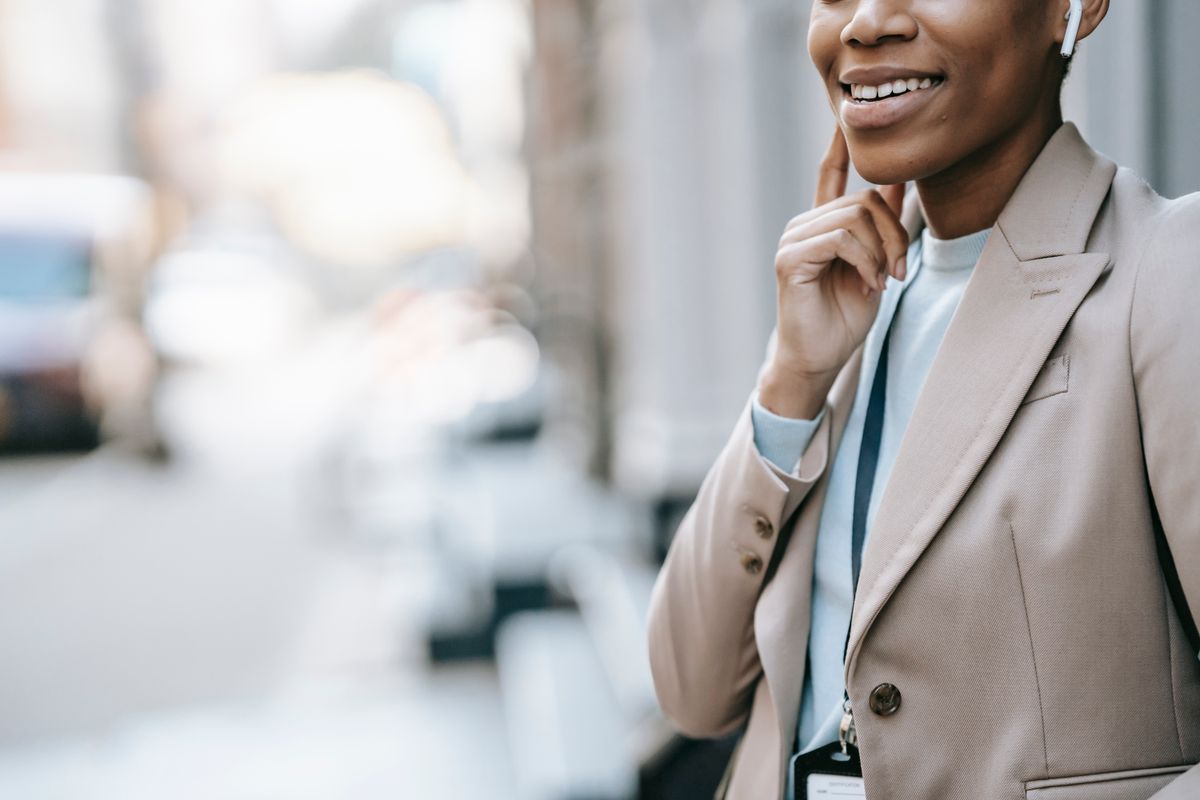 Crop anonymous content young female in formal jacket with badge listening to music using wireless earphones
