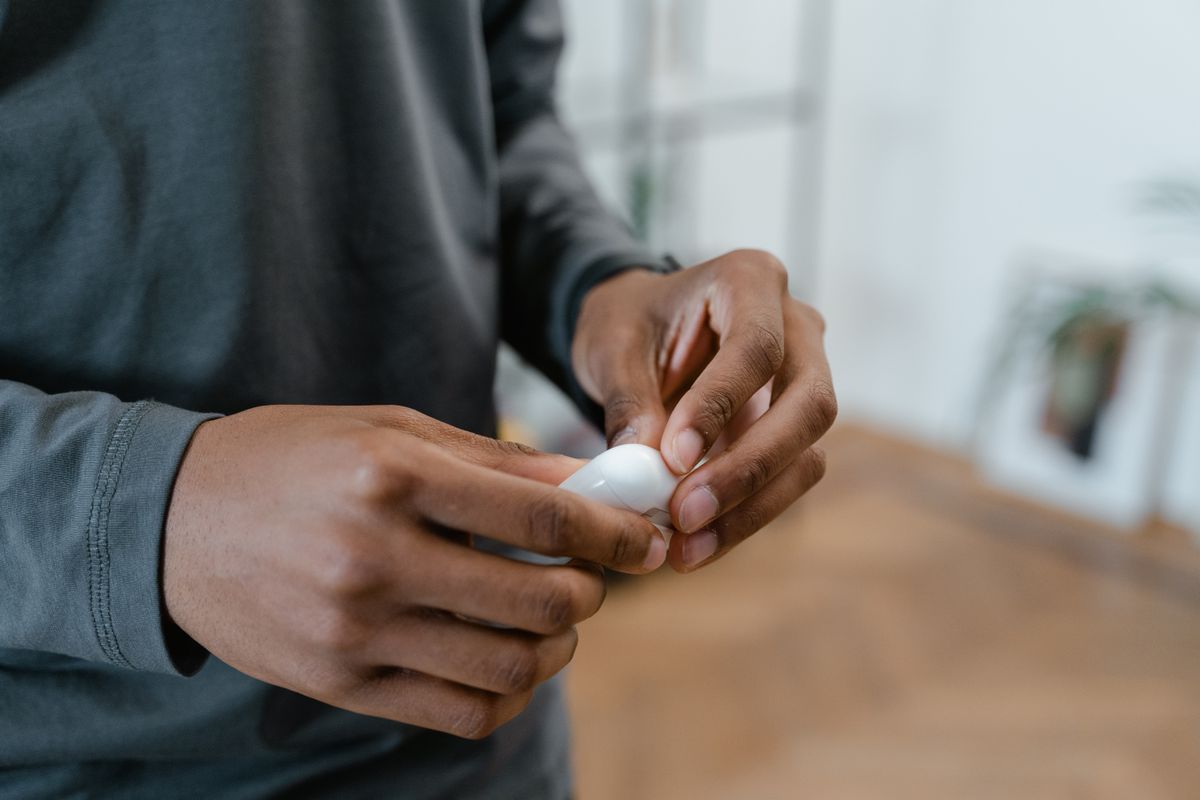 A person holding wireless earbuds in their hands. Indoors with blurred background.