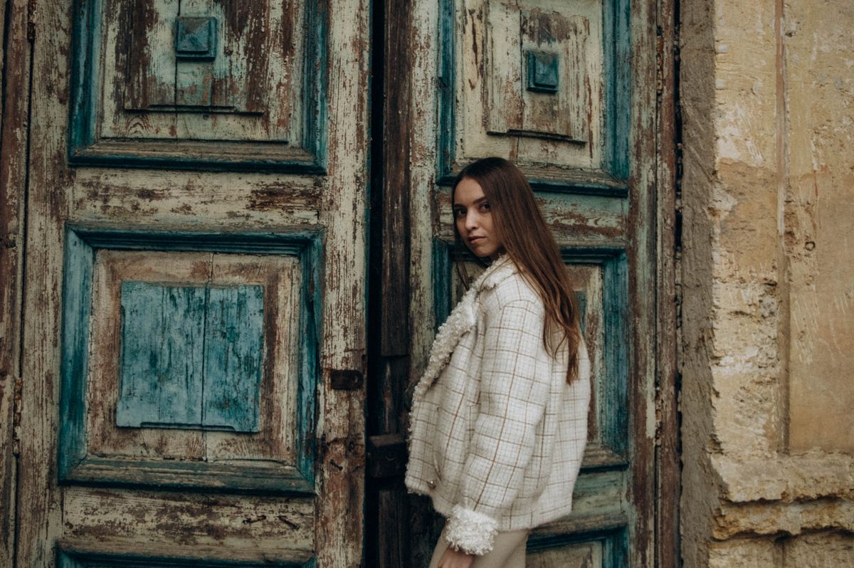 A fashionable woman poses in a vintage jacket against a weathered wooden door, exuding style and elegance.
