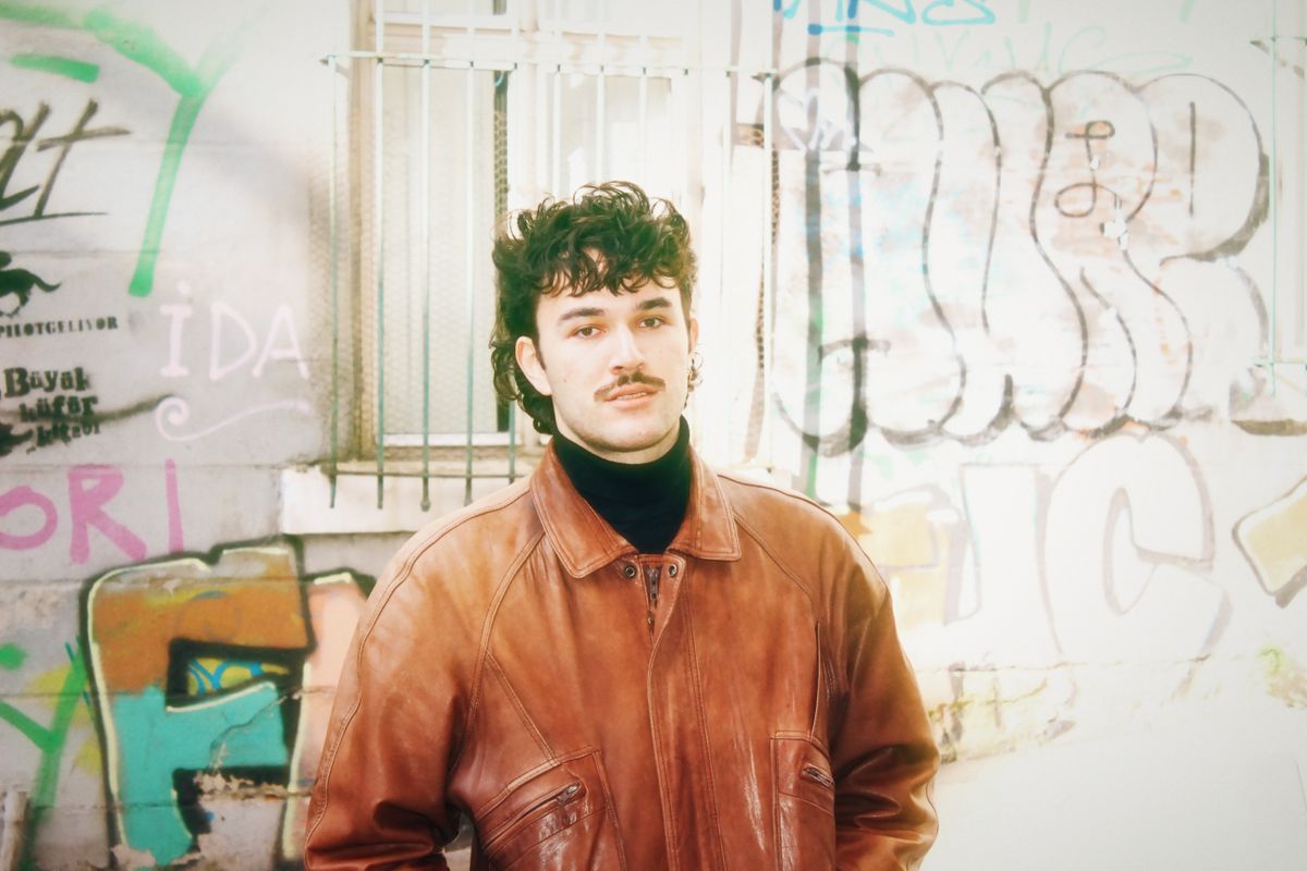 Young man in brown leather jacket standing in front of vibrant graffiti wall. Urban style.