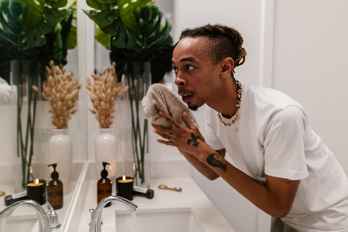 A man using a towel for skincare in a stylish and well-lit bathroom setting.