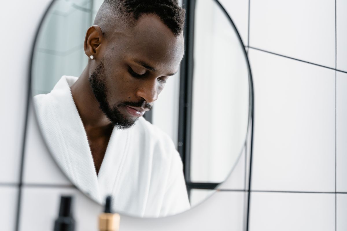 A thoughtful man looks down at his reflection in a modern bathroom mirror.