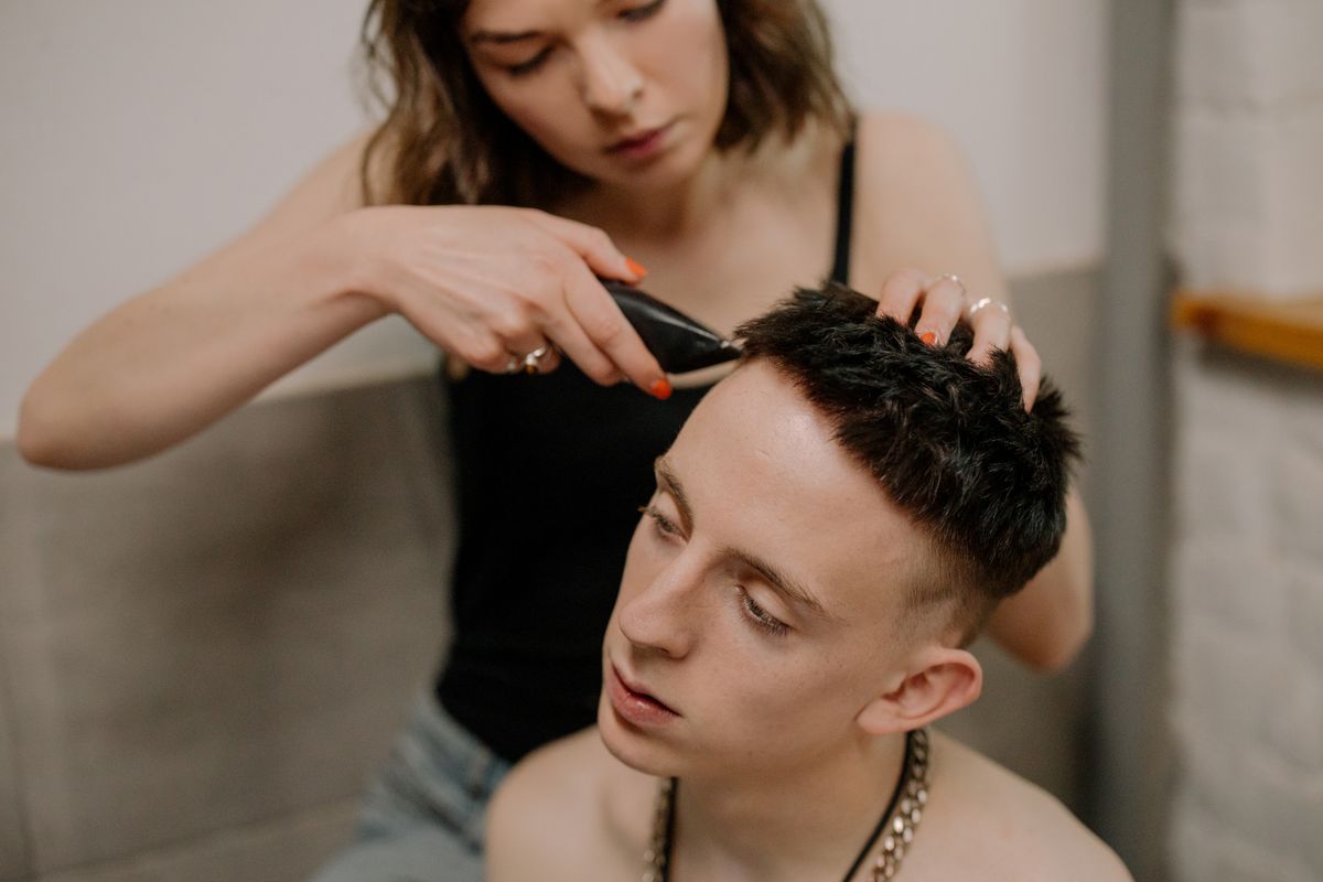 A woman gives a haircut to a young man at home, focusing on personal grooming and DIY skills.