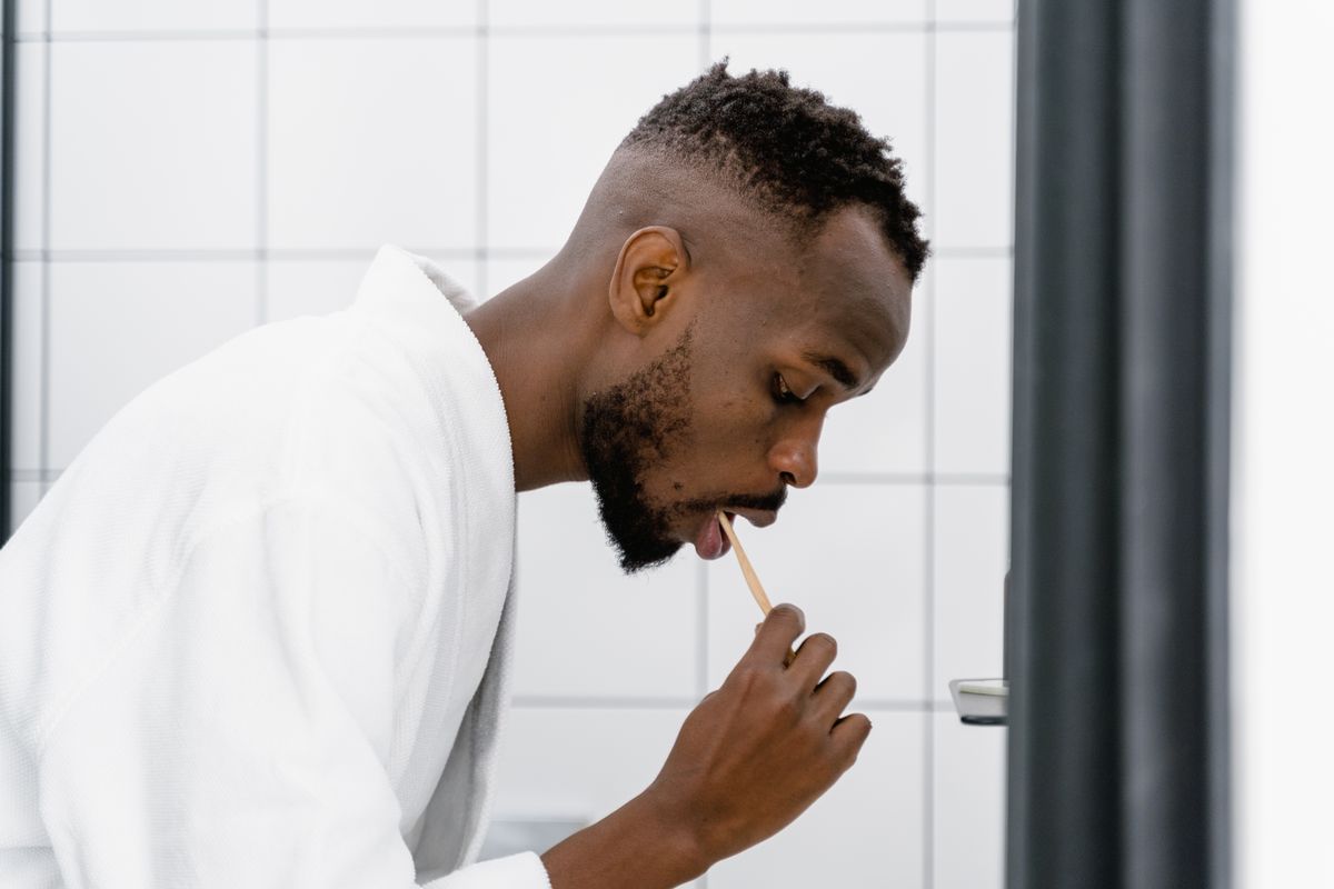 Adult man in a bathrobe brushing teeth in a modern bathroom setting.
