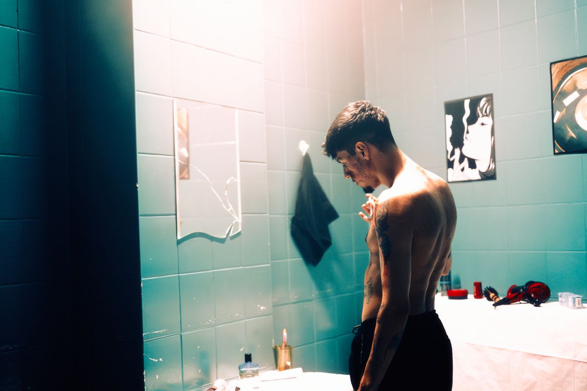 Shirtless man in a modern bathroom, captured in a moody, artistic style with dramatic lighting.